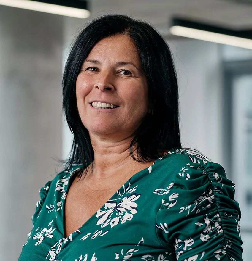 Woman wearing green floral blouse smiling indoors.