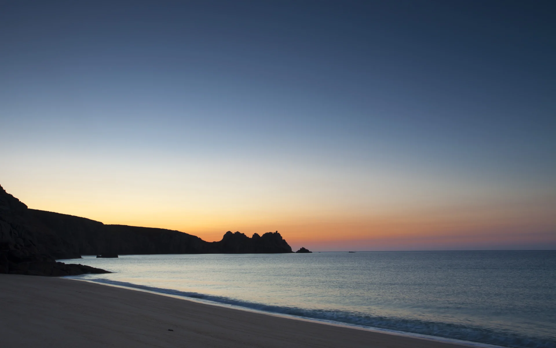 Sunset over a tranquil beach with cliffs.