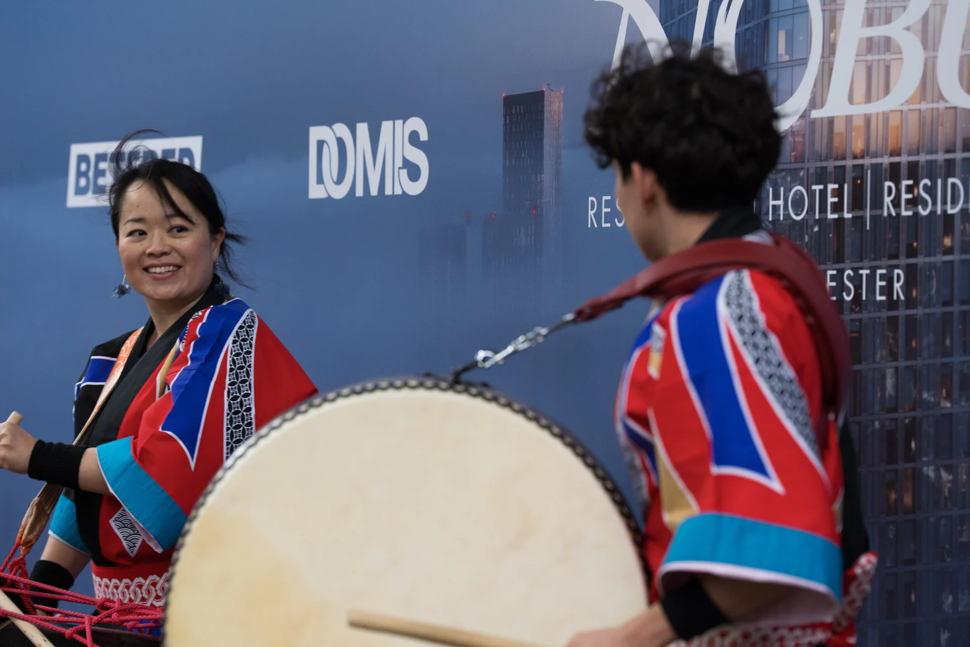 Two performers in colorful costumes playing drums.