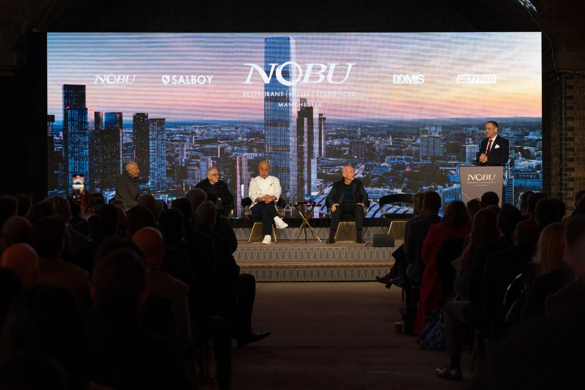 Panel discussion at Nobu event with cityscape backdrop.