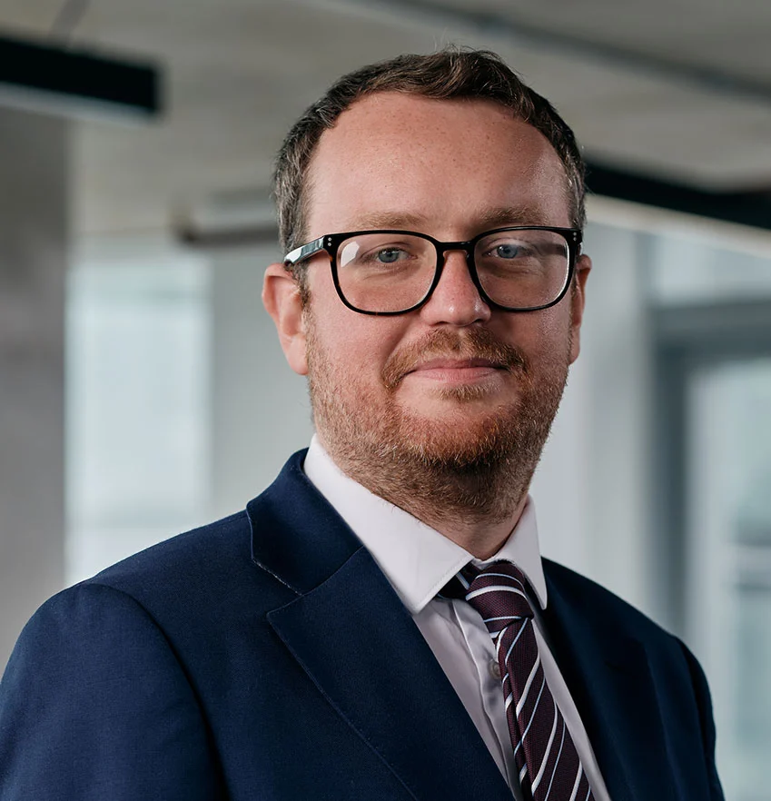 Man in suit and glasses smiling indoors.