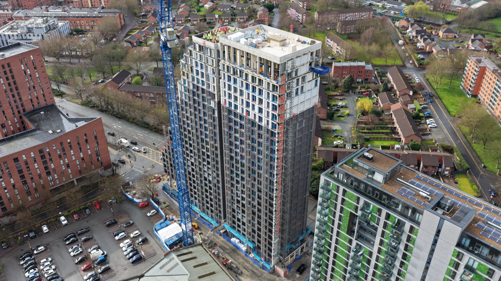 High-rise building under construction with crane and neighborhood.