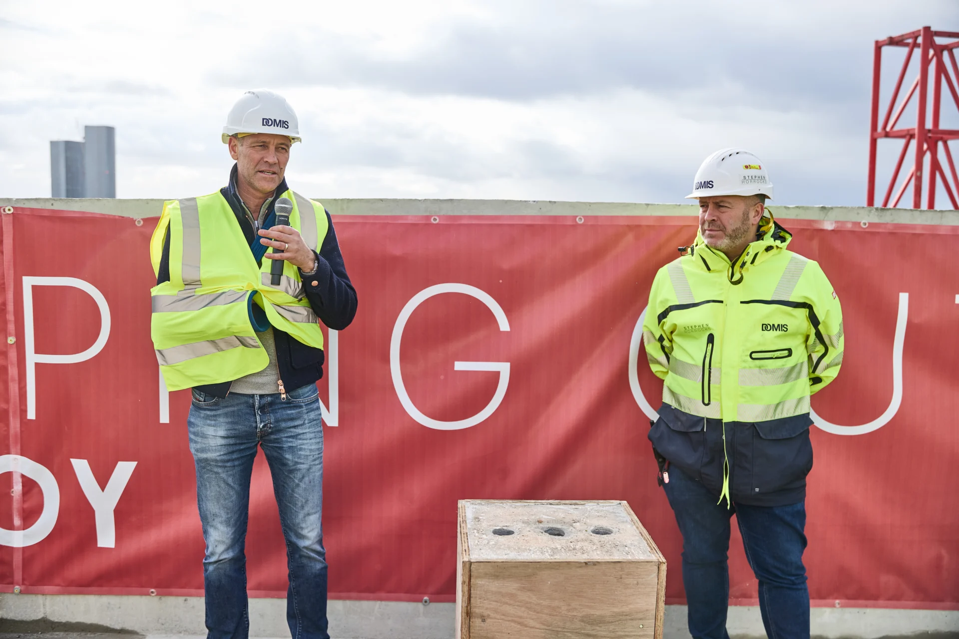 Two construction workers in safety gear speaking.